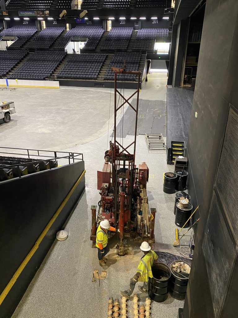 Geotechnical drilling crew operating rig inside arena during subsurface investigation for foundation evaluation
