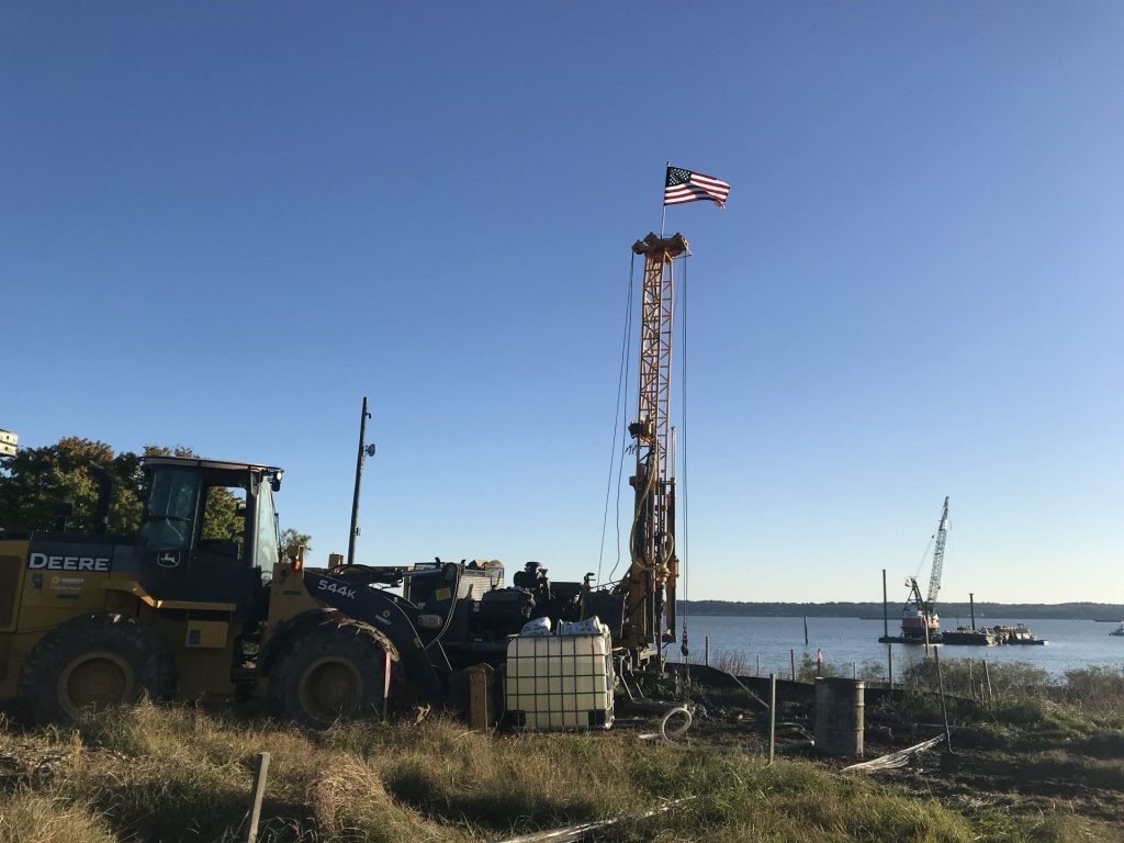 Geotechnical drilling rig performing subsurface investigation at waterfront location with equipment and crew on site